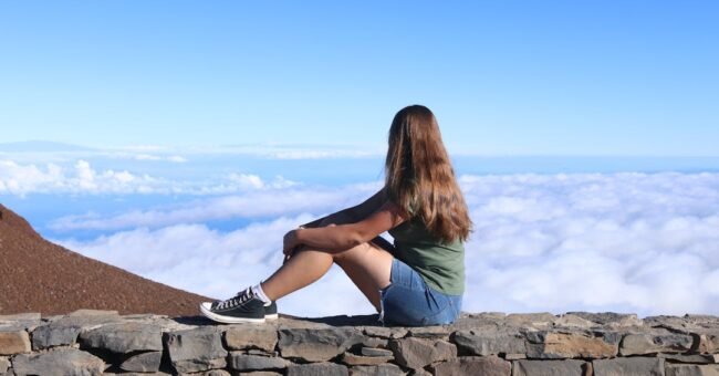 Young traveler sitting above the clouds, representing independent travel websites, slow travel and thoughtful travel planning.