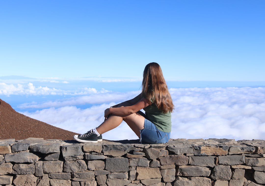 Young traveler sitting above the clouds, representing independent travel websites, slow travel and thoughtful travel planning. 
