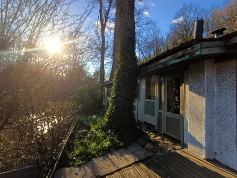 Off-grid wooden chalet beside the Aisne river in rural Durbuy, Belgium, surrounded by trees at sunset