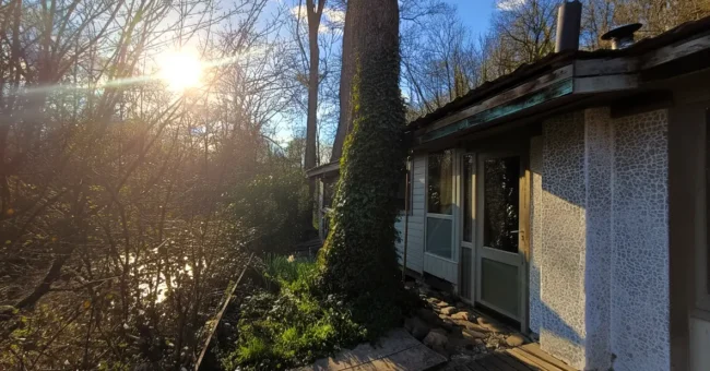 Off-grid wooden chalet beside the Aisne river in rural Durbuy, Belgium, surrounded by trees at sunset