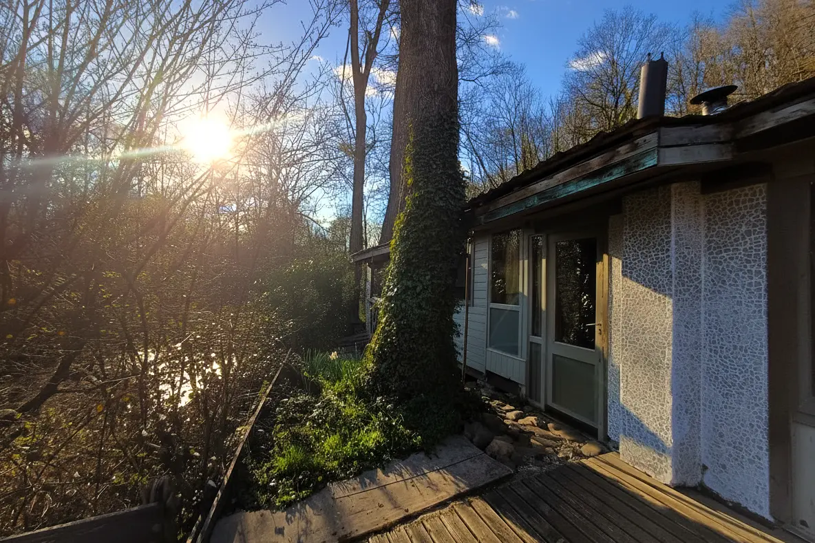 Off-grid wooden chalet beside the Aisne river in rural Durbuy, Belgium, surrounded by trees at sunset