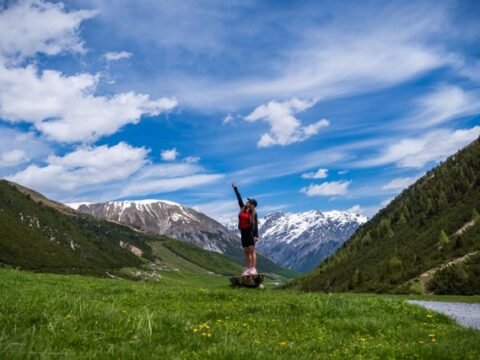 Summer landscape of Livigno in the Italian Alps, with green meadows, alpine houses and snow-covered mountains under a blue sky.