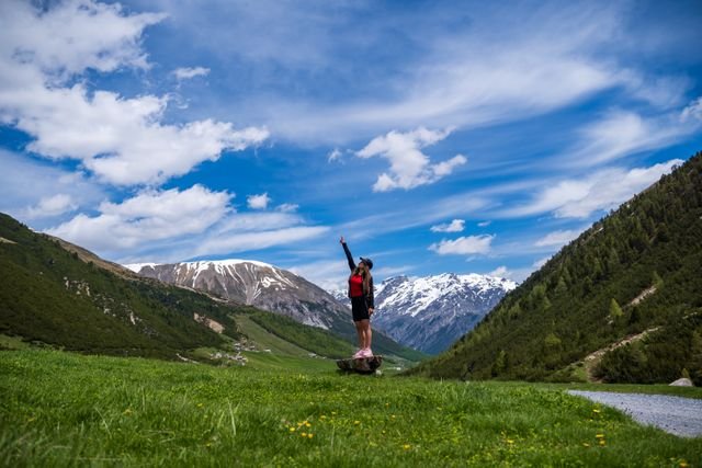 Summer landscape of Livigno in the Italian Alps, with green meadows, alpine houses and snow-covered mountains under a blue sky.