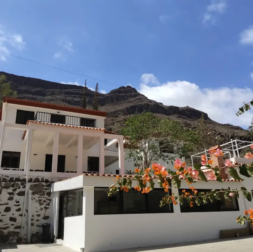 White Aya House retreat centre beneath the mountains near Maspalomas, Gran Canaria, with flowering bougainvillea and blue sky