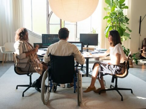 A diverse group taking part in a collaborative meeting in an accessible workplace, including a wheelchair user. Featured image for the Voluntouring.org guide about inclusive volunteering, accessibility, flexible participation and removing barriers for volunteers.