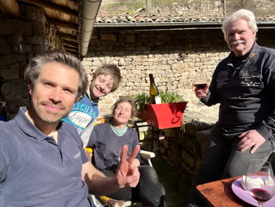 A family and guest spending time together outside a stone house during a rural volunteer exchange in Ardèche