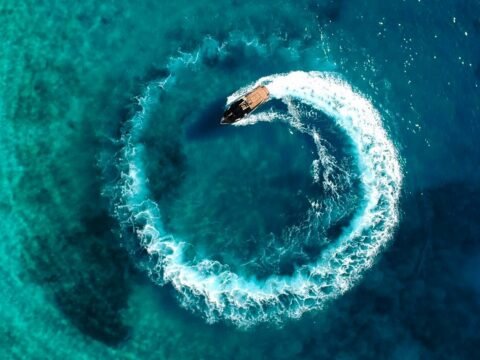 Aerial view of a motorboat on turquoise water during a coastal tourism work exchange in Himara, Albania