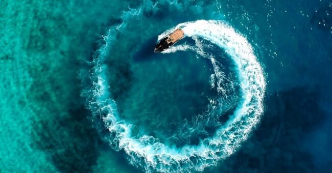 Aerial view of a motorboat on turquoise water during a coastal tourism work exchange in Himara, Albania