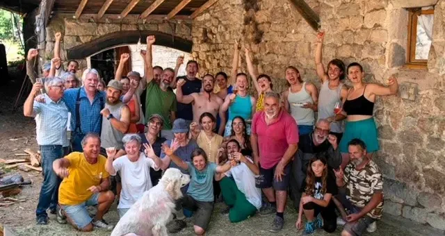 Group of volunteers, friends and family outside a stone farm building during a farm volunteering experience in Ardèche, France