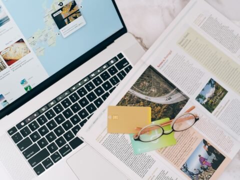 A travel planning flat lay with a laptop, map, credit cards and eyeglasses. Featured image for the Voluntouring.org guide about volunteer abroad costs, participation fees, cost-recovery contributions and what travellers should check before paying for a volunteer program.