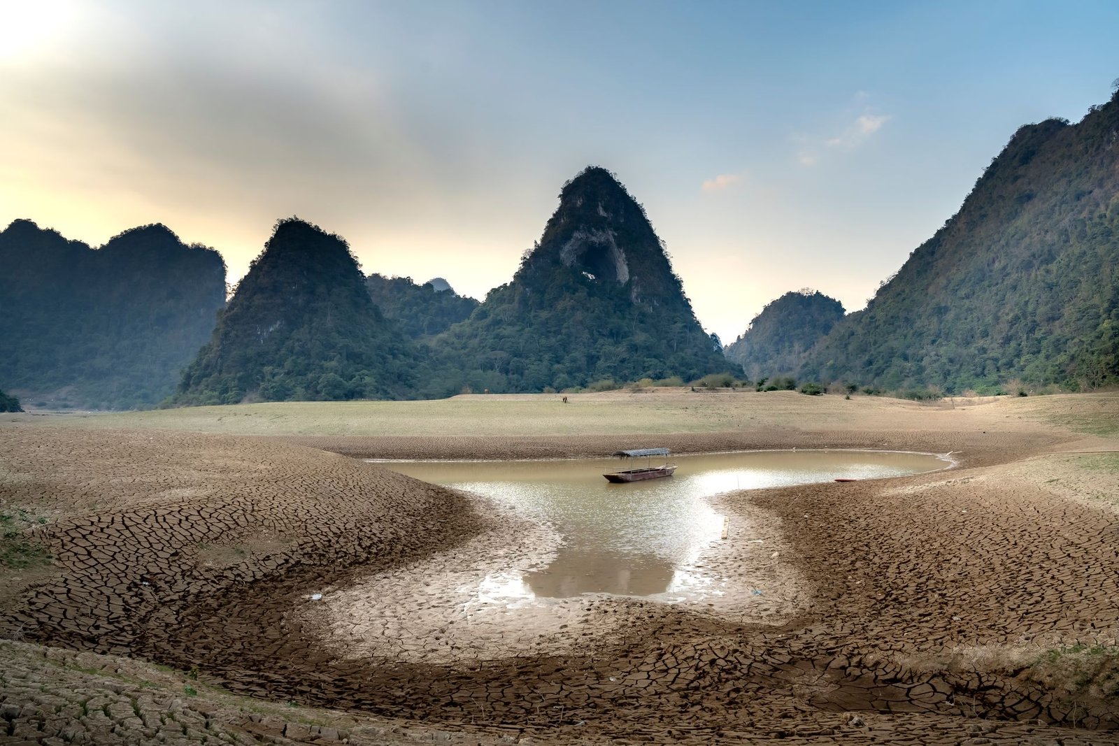 Climate change and drought: cracked earth surrounding a nearly dry mountain lake, with a small boat in the remaining water